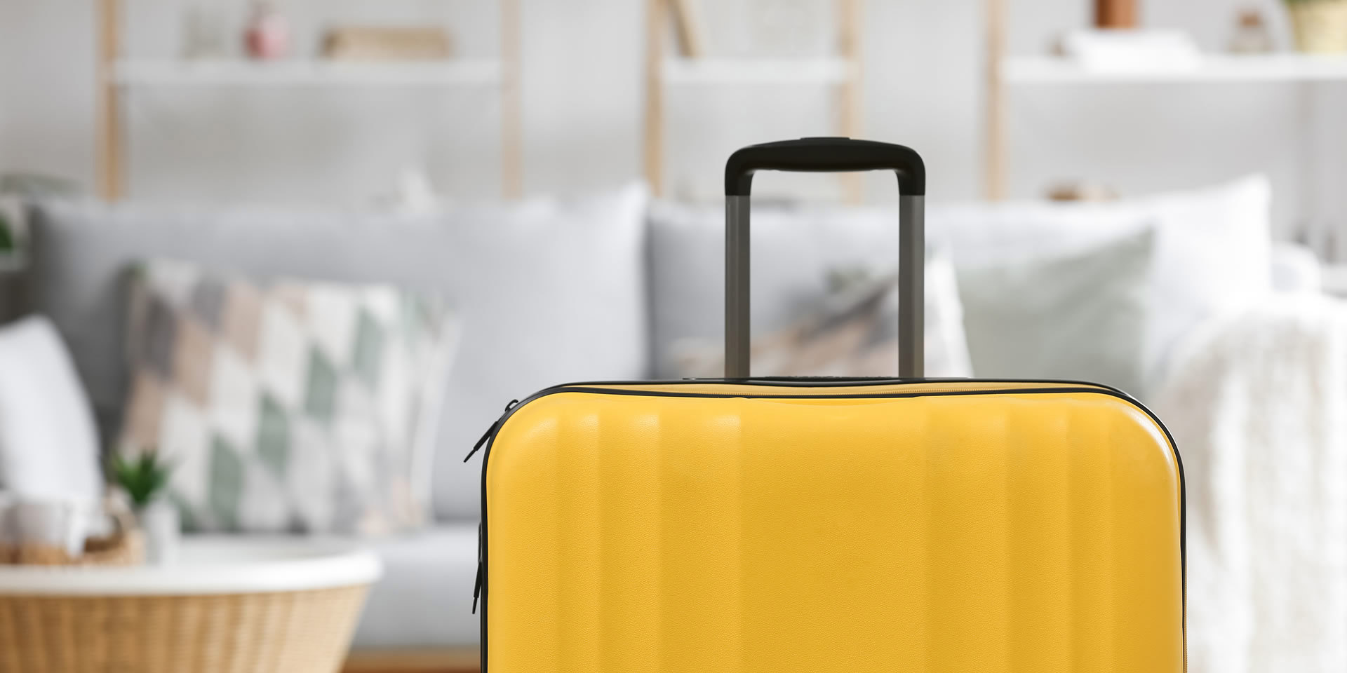 Bright yellow suitcase standing indoors, with a sofa and shelves visible in the background.