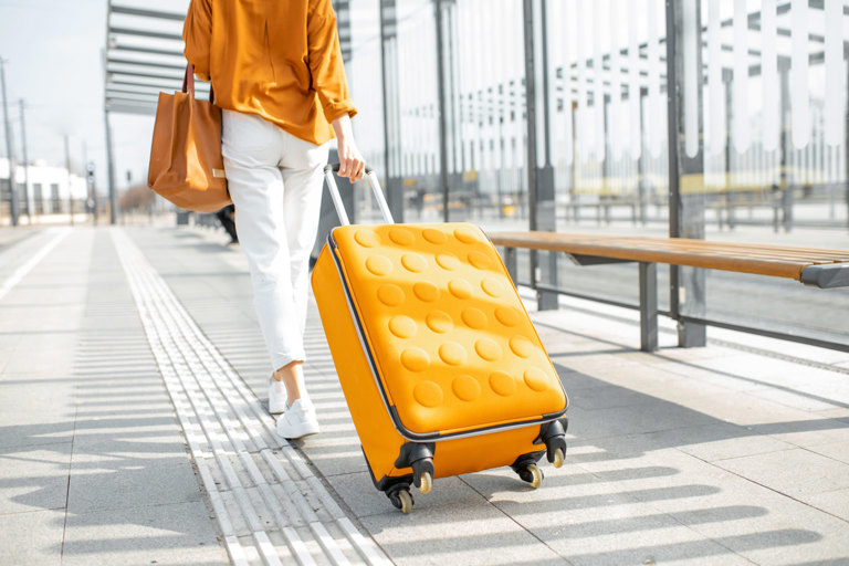Person walking along a platform while pulling a bright yellow wheeled suitcase.